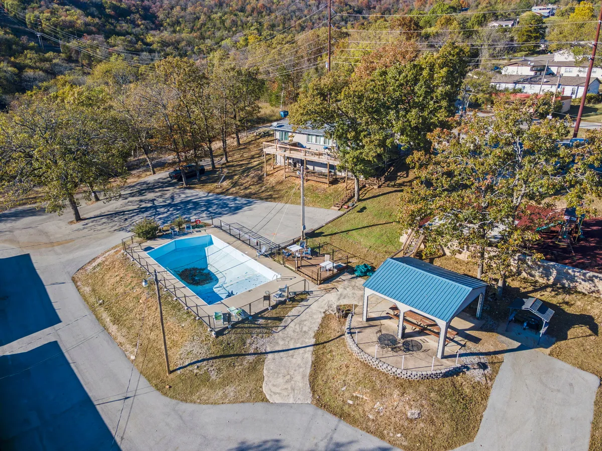 A sparkling swimming pool is surrounded by lush trees, an inviting gazebo, and a convenient parking area nearby. The area is designed for relaxation, swimming, and socializing outdoors.