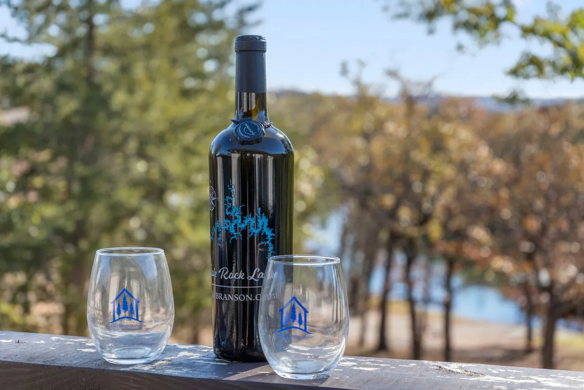 At sunset, a wine bottle and two glasses are set atop a wooden deck with the lake stretching out beyond, creating an atmosphere of relaxed lakeside enjoyment and intimate gatherings as day turns to evening.