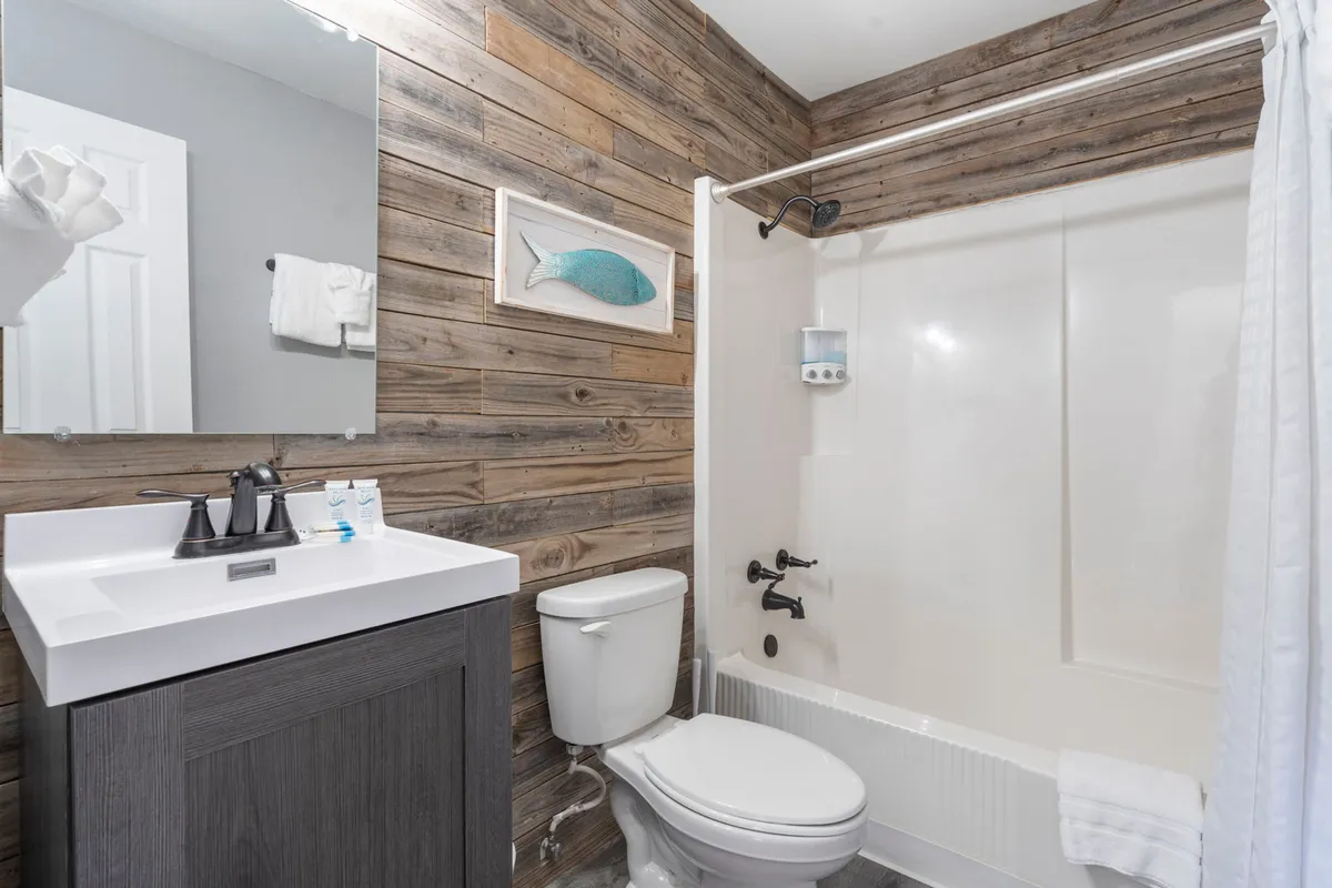 A bathroom features stylish wooden wall paneling, a modern sink and vanity, framed fish artwork, and a glimpse of the shower area, blending function with a soothing, spa-like atmosphere.