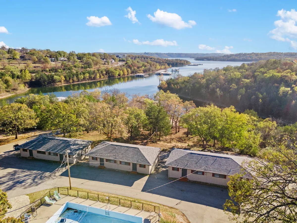 An inviting exterior shot showcasing the swimming pool surrounded by trees, with cabins and the tranquil lake in the background. The scene conveys an atmosphere of relaxation and abundant recreational opportunities for all ages.