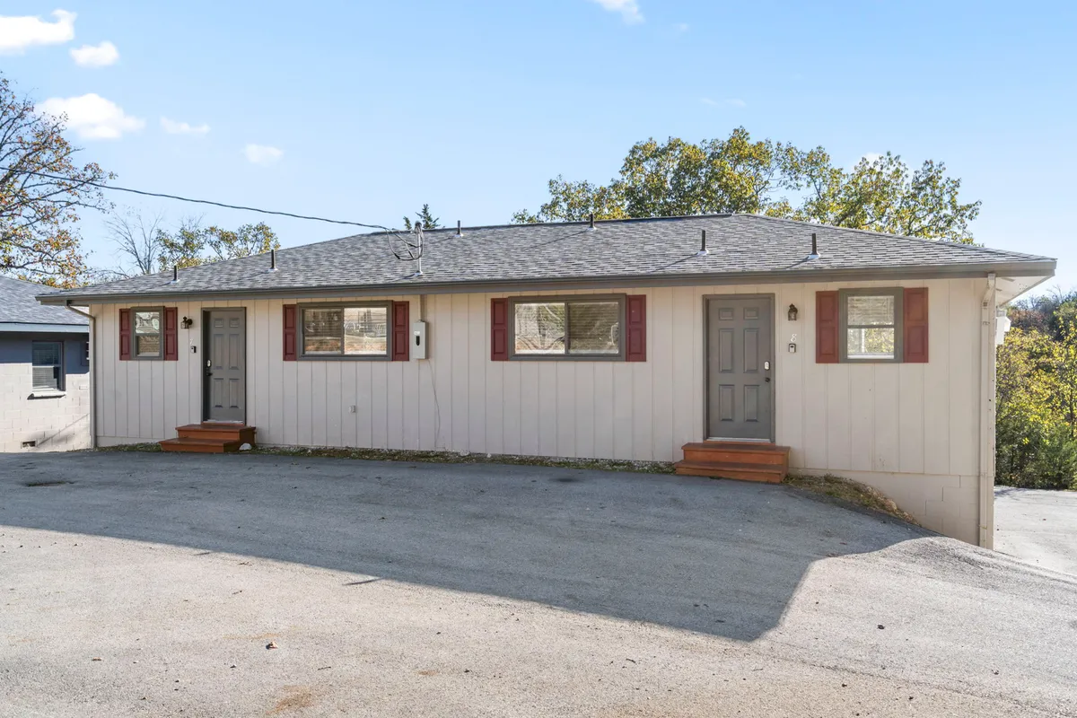 A welcoming exterior view of Kimberling Star - 8, with two inviting front doors, a well-maintained driveway, and mature trees framing the property. The scene radiates a serene, comfortable atmosphere ideal for arriving guests and their pets.
