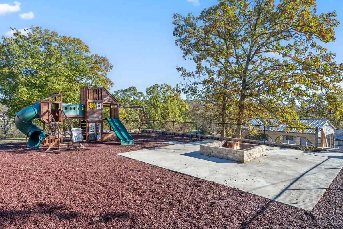 This image features a vibrant playground structure adjacent to a welcoming fire pit, surrounded by mature trees. The setup is perfect for family gatherings, with spaces for children to play and adults to relax or roast marshmallows together.