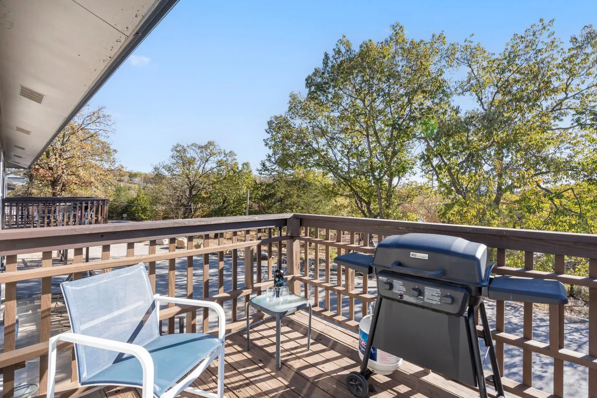 An outdoor area featuring a grill, an inviting chair, and a scenic view of trees just beyond the deck, suggesting a relaxed, open-air setting perfect for unwinding after lakeside adventures with a pet.