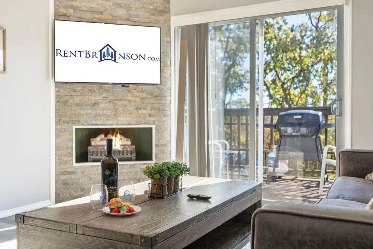 A view of the living space centered around a fireplace and television, with a coffee table and a decorative plant. Sliding glass doors open onto a deck, offering a glimpse of the outdoors and emphasizing the connection between the interior and the private deck.