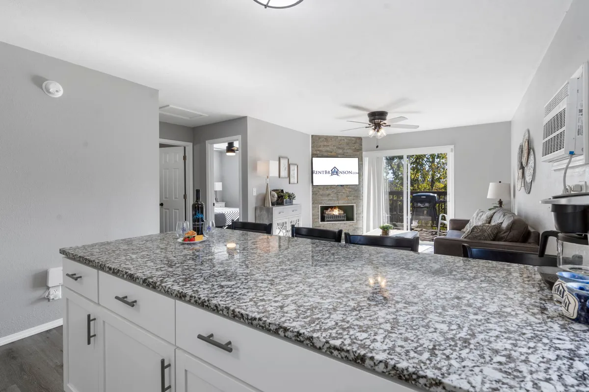 A granite countertop extends from the kitchen into an open living area, with a fireplace in view. This space balances functionality for cooking with comfort for entertaining, emphasizing the kitchen's connection to the rest of the home.