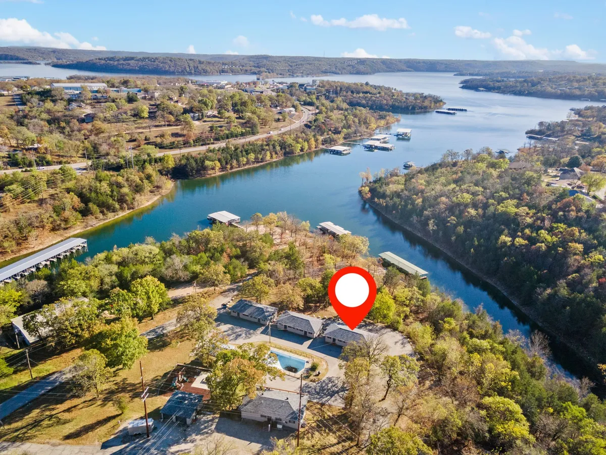 A broad view of the sparkling lake, bordered by trees, with glimpses of a swimming pool and nearby houses. The tranquil setting evokes opportunities for long walks, swimming, and exploring the natural surroundings.